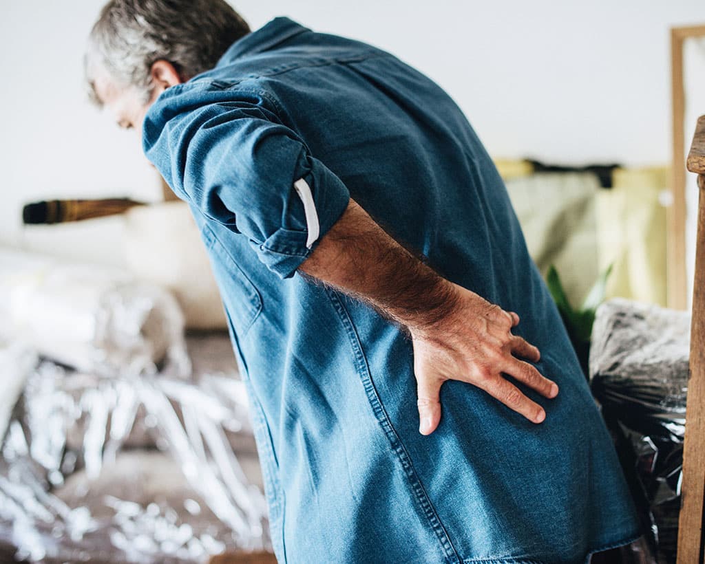 Mann mit akutem Hexenschuss hält sich den unteren Rücken in der Physiotherapiepraxis Gesundheitsreich Lübeck